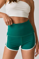 Woman wearing high-waist red shorts with white contrast piping. / Woman wearing high-waist green shorts with white contrast piping.