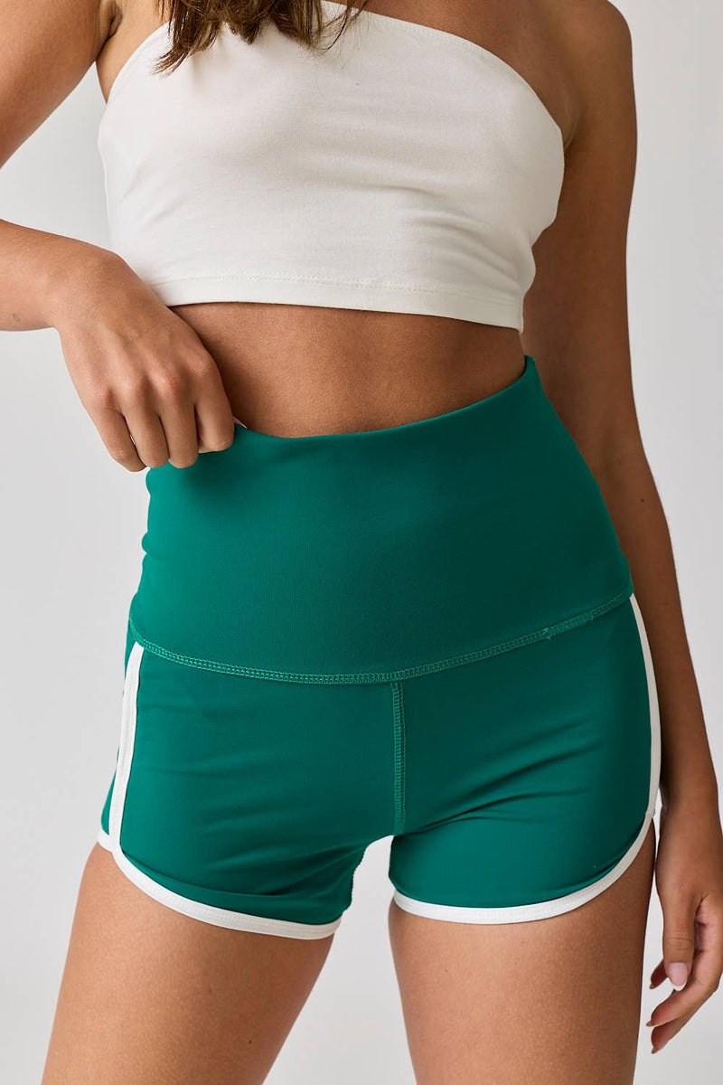 Woman wearing high-waist red shorts with white contrast piping. / Woman wearing high-waist green shorts with white contrast piping.