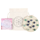 Seed of Life Crystal Grid Set featuring 6 sodalite tumblestones, 5 aventurine tumblestones, 1 clear quartz tumblestone, and an engraved wooden grid, surrounded by candles and decorative flowers.