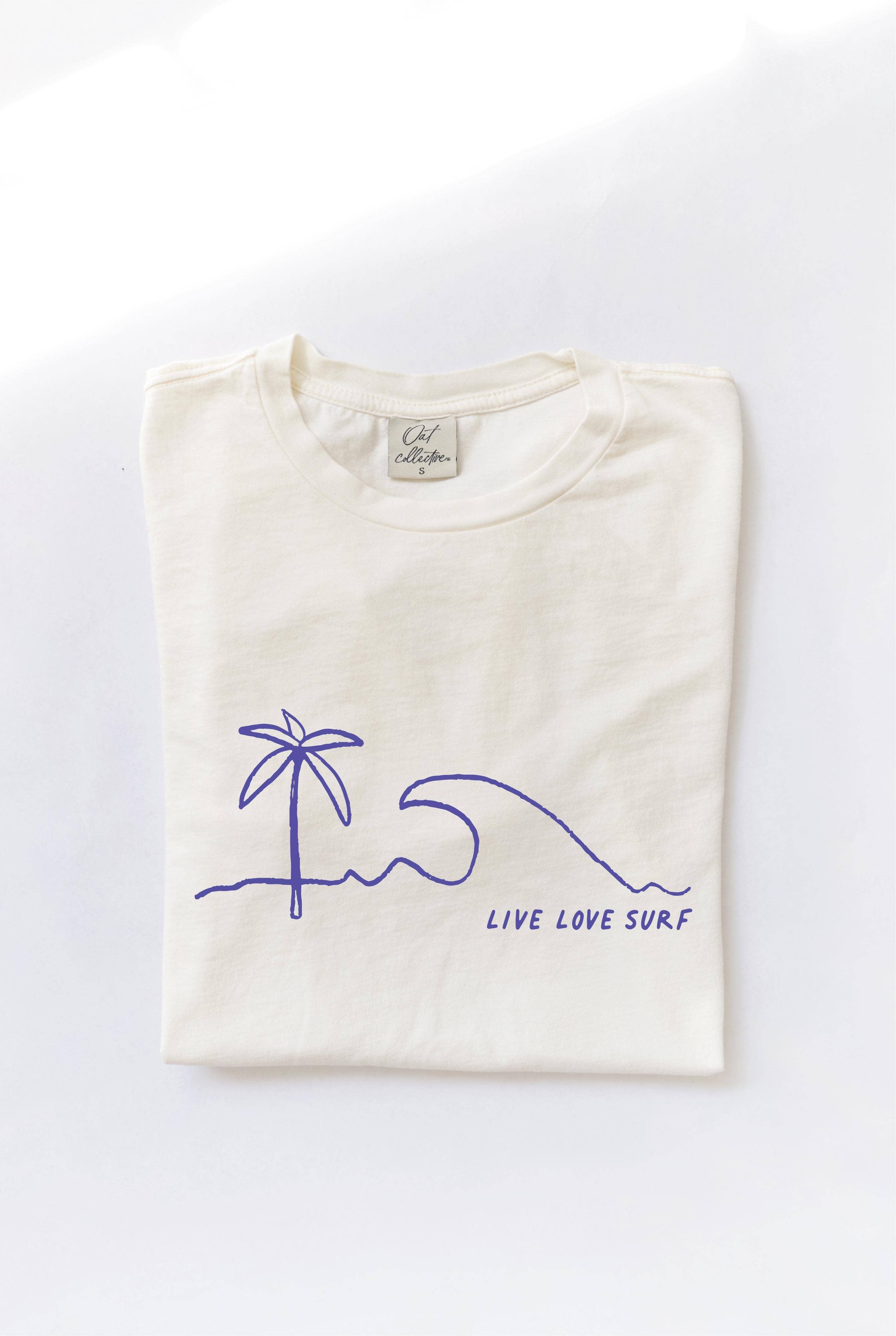 Folded cream-colored t-shirt with a blue minimalist palm tree, wave, and "LIVE LOVE SURF" graphic.
