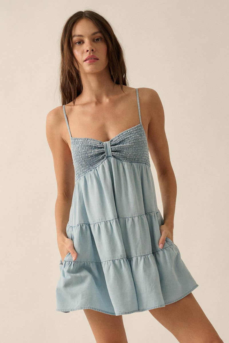 Woman wearing a light blue smocked romper with spaghetti straps and tiered flowy shorts.