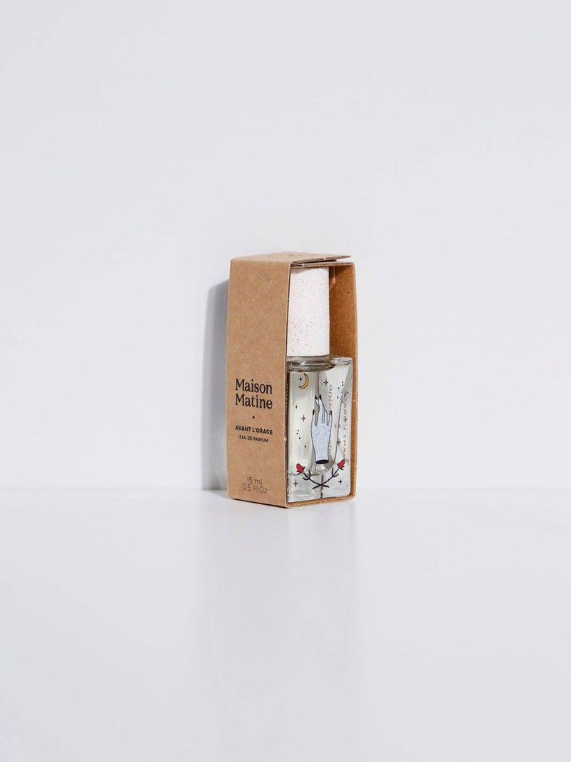 Maison Matine Avant l’Orage perfume bottle with celestial illustrations, placed among citrus fruits and sample vials on blue fabric