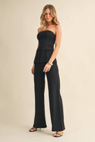 Woman wearing a black strapless jumpsuit on a beige background