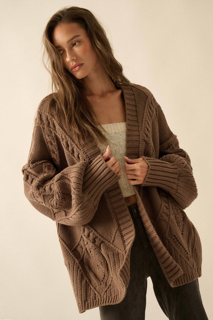 Woman wearing a brown cable knit cardigan against a plain background