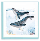 Quilled design of two whales on a watercolor background with a light blue border
