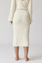 Woman wearing a white round neck long sleeve crop soft knit top and midi skirt set with a side slit.