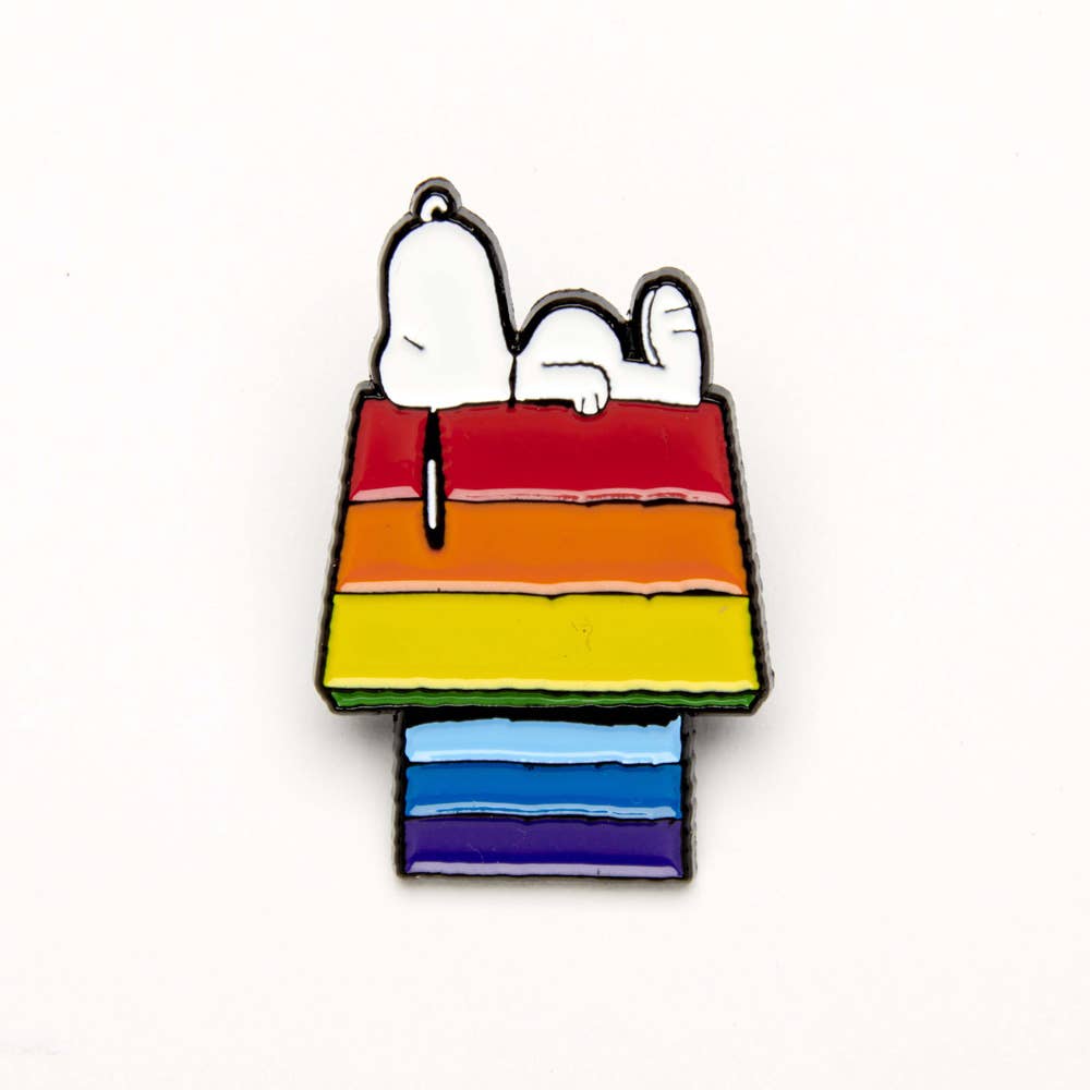 Enamel pin featuring Snoopy lying on a rainbow-striped doghouse, designed with vibrant colors and playful details