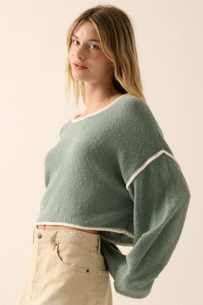 Woman wearing a sage green off-shoulder cropped sweater with white trim details and long sleeves.