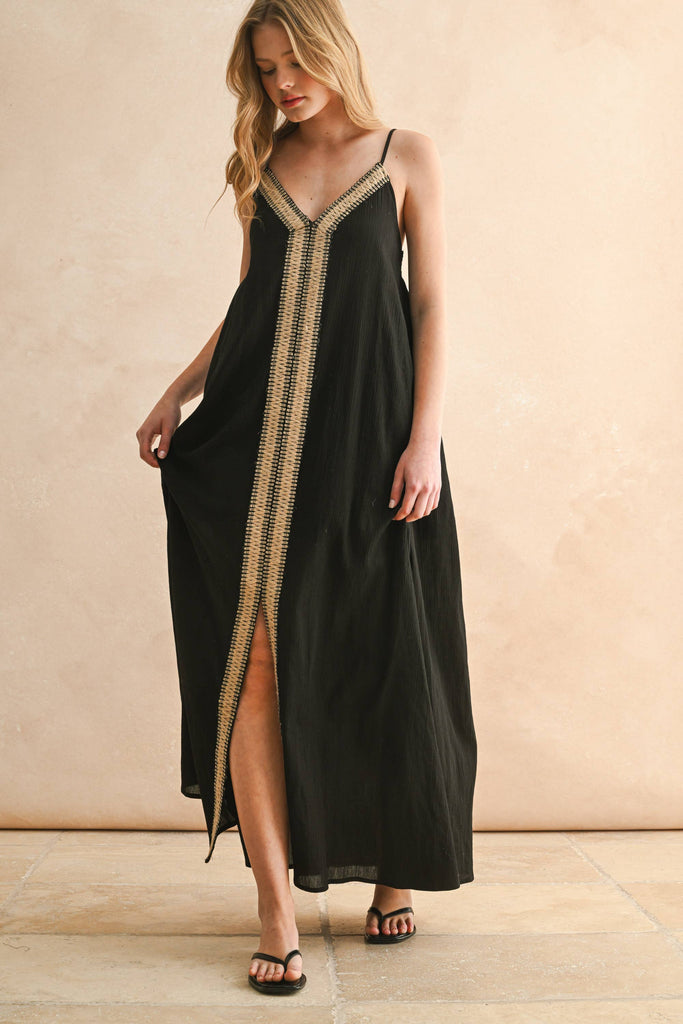 Model in black embroidered maxi dress with thin straps and flowy silhouette, featuring beige V-shaped stitching detail.