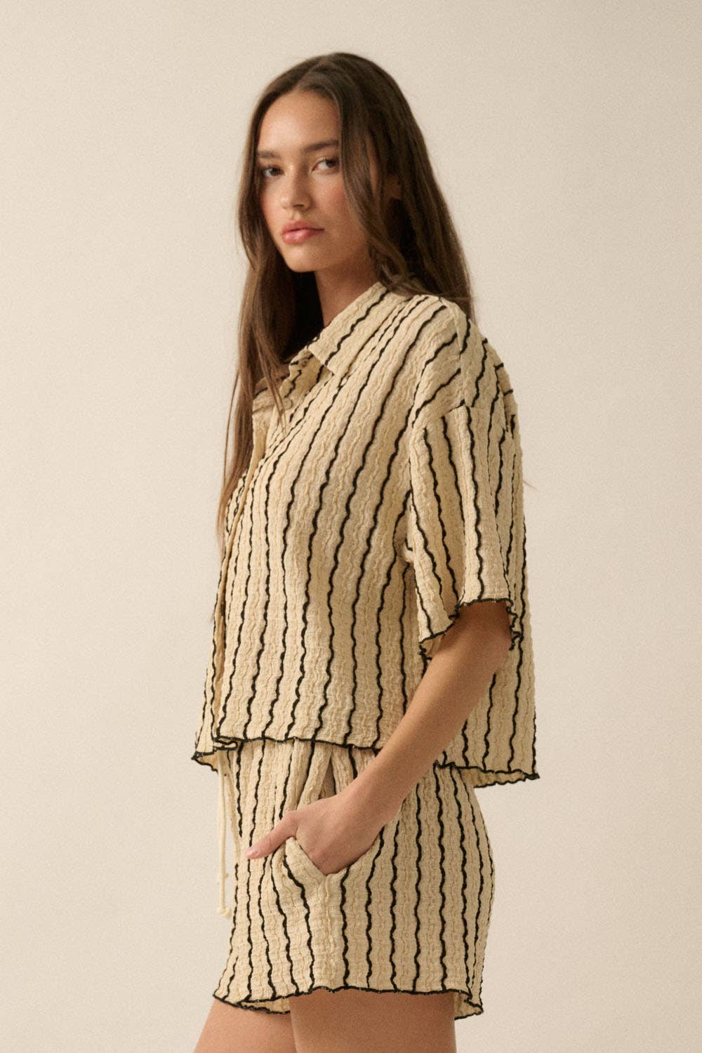 Woman wearing a beige striped two-piece lounge set with button-up shirt and matching drawstring shorts.