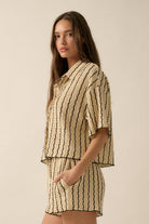 Woman wearing a beige striped two-piece lounge set with button-up shirt and matching drawstring shorts.