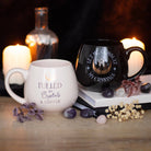 Black mug with ‘Let Me Consult My Crystals’ text and a gold foil crescent moon and crystal design, placed among crystals.