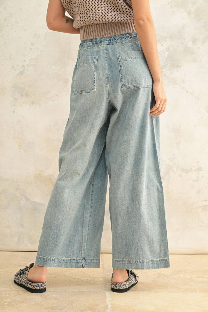 Woman wearing light wash wide-leg denim pants with elastic drawstring waist and front patch pockets.