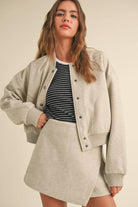 Model wearing a wool-blend jacket and mini skirt set in a neutral tone, styled with a striped tee and relaxed fit, showcasing casual elegance.