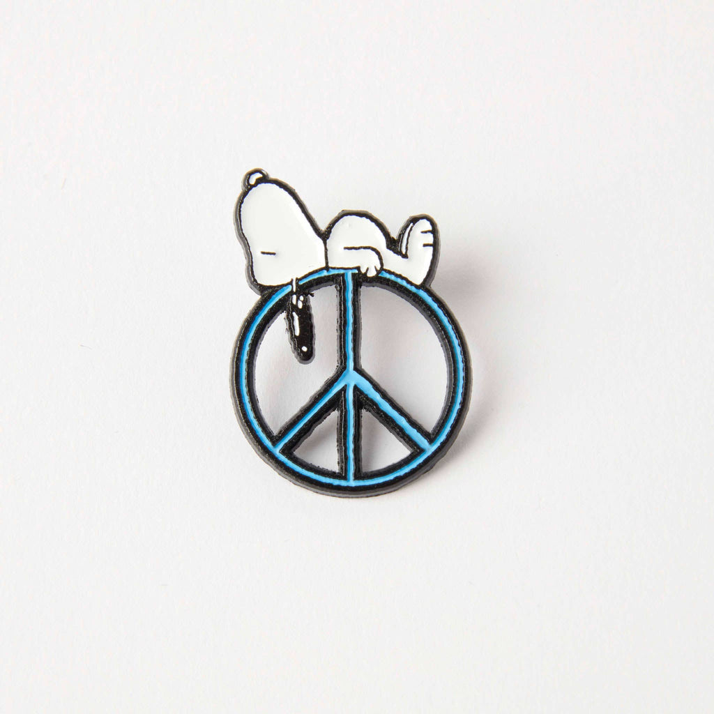 Enamel pin of Snoopy resting on a blue peace sign, designed with a minimalist and whimsical style.