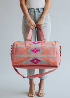 Woman holding a pink and orange woven weekender duffel bag with fuchsia geometric design