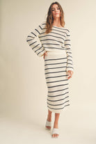 Woman wearing a high-waisted, ivory and black striped knit midi skirt with slide sandals.