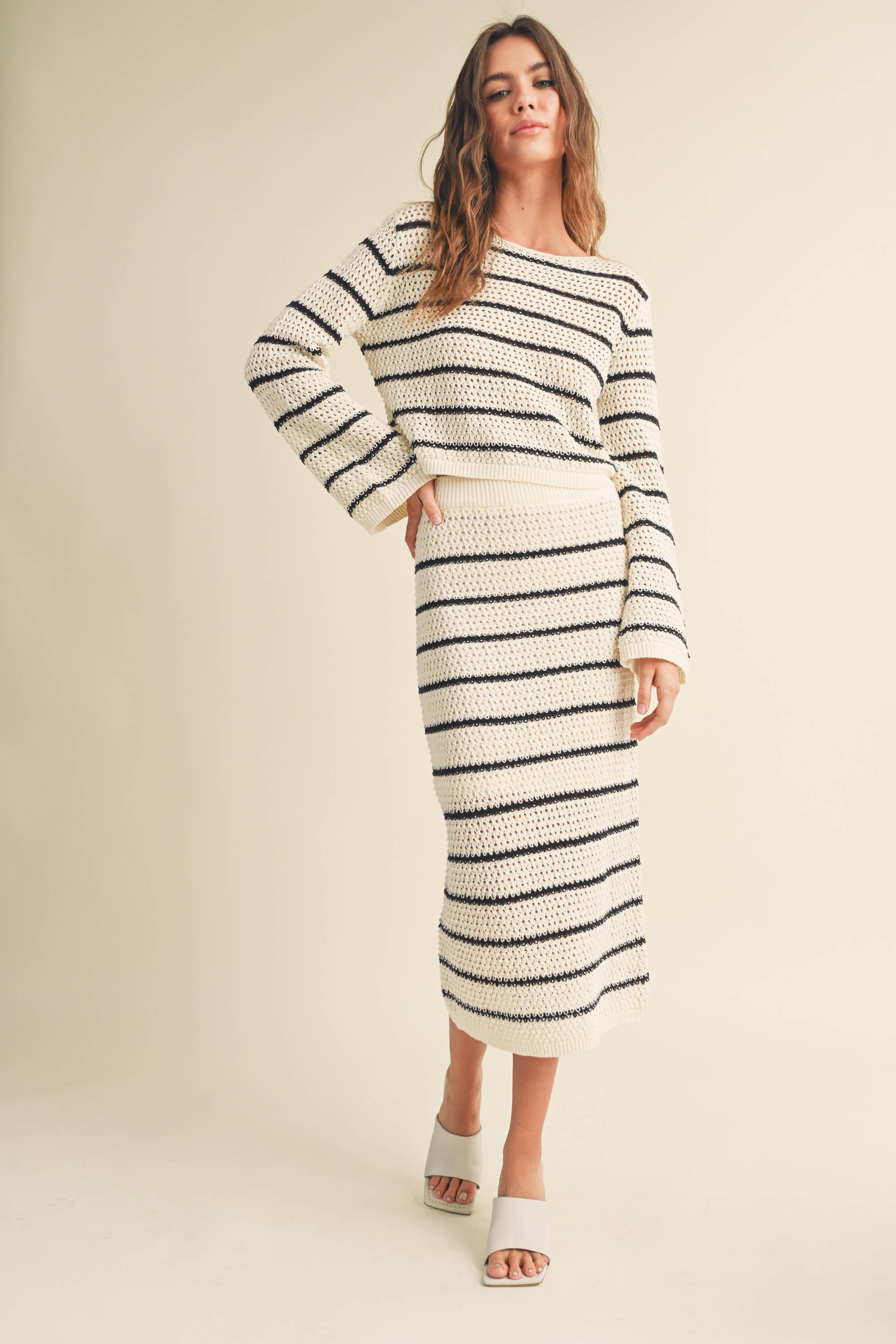 Woman wearing a high-waisted, ivory and black striped knit midi skirt with slide sandals.