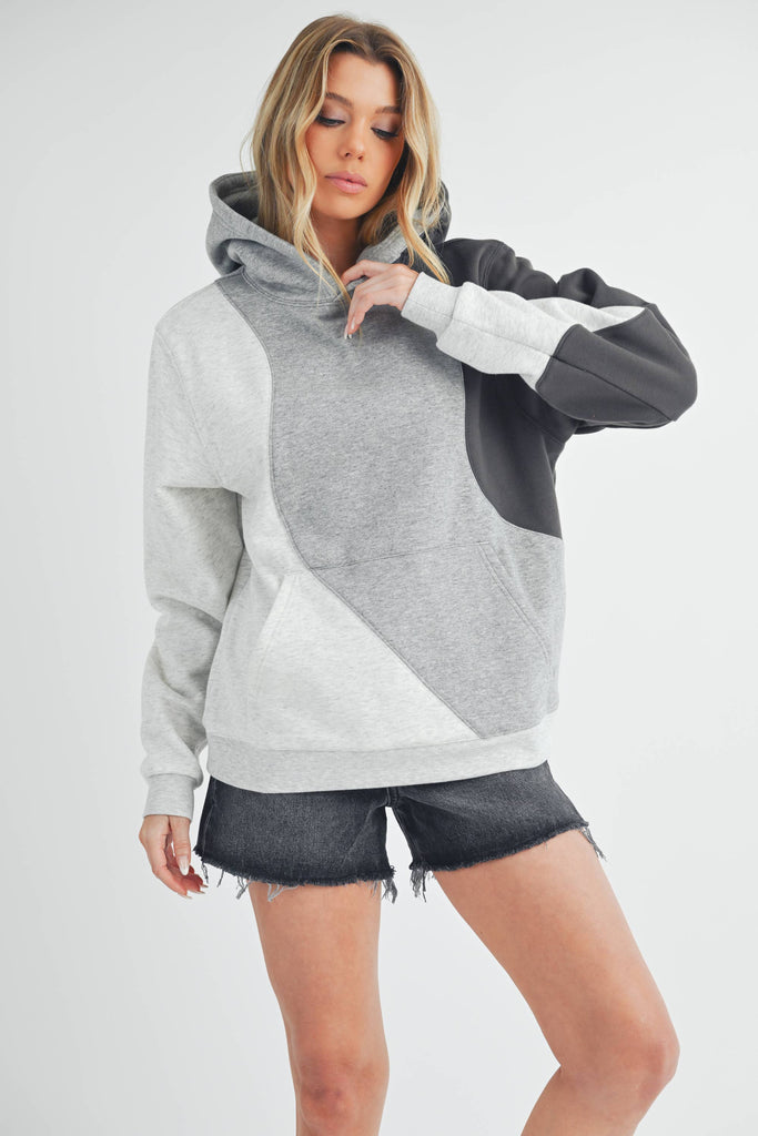 Woman wearing an oversized colorblock hoodie in grey, black, and ivory with a relaxed fit and kangaroo pocket.