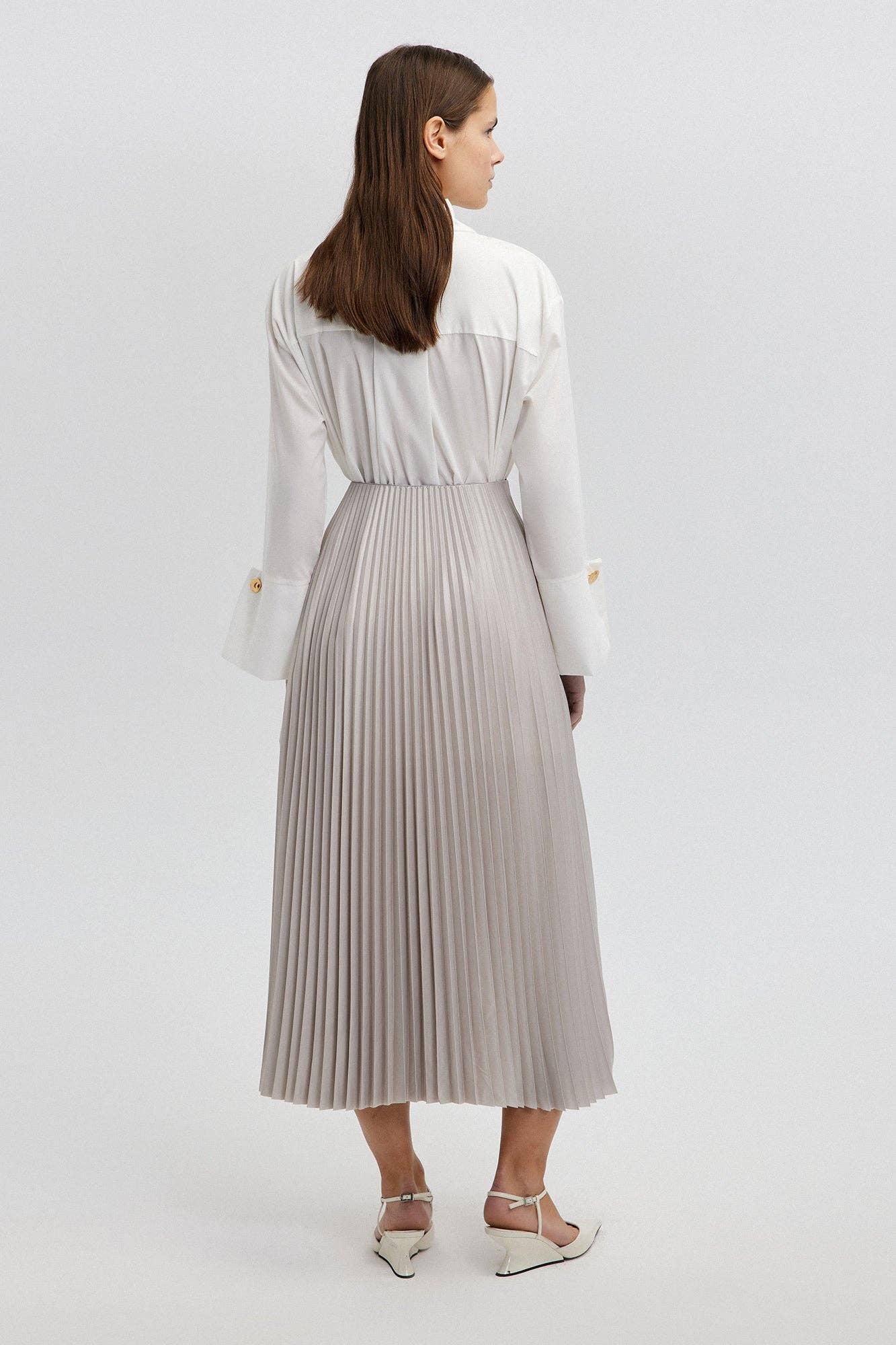 Model wearing a high-waisted pleated maxi skirt styled with a white blouse and pointed heels.