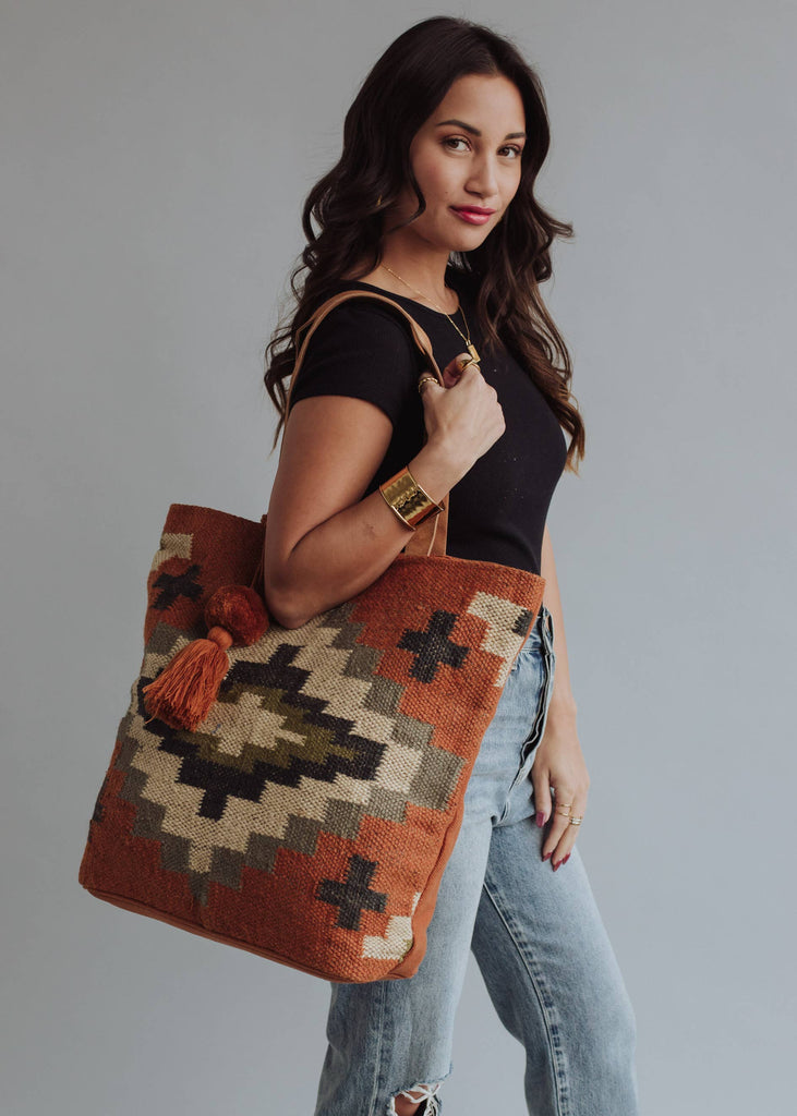 Woman holding a rust and olive green diamond-patterned woven tote with tassel