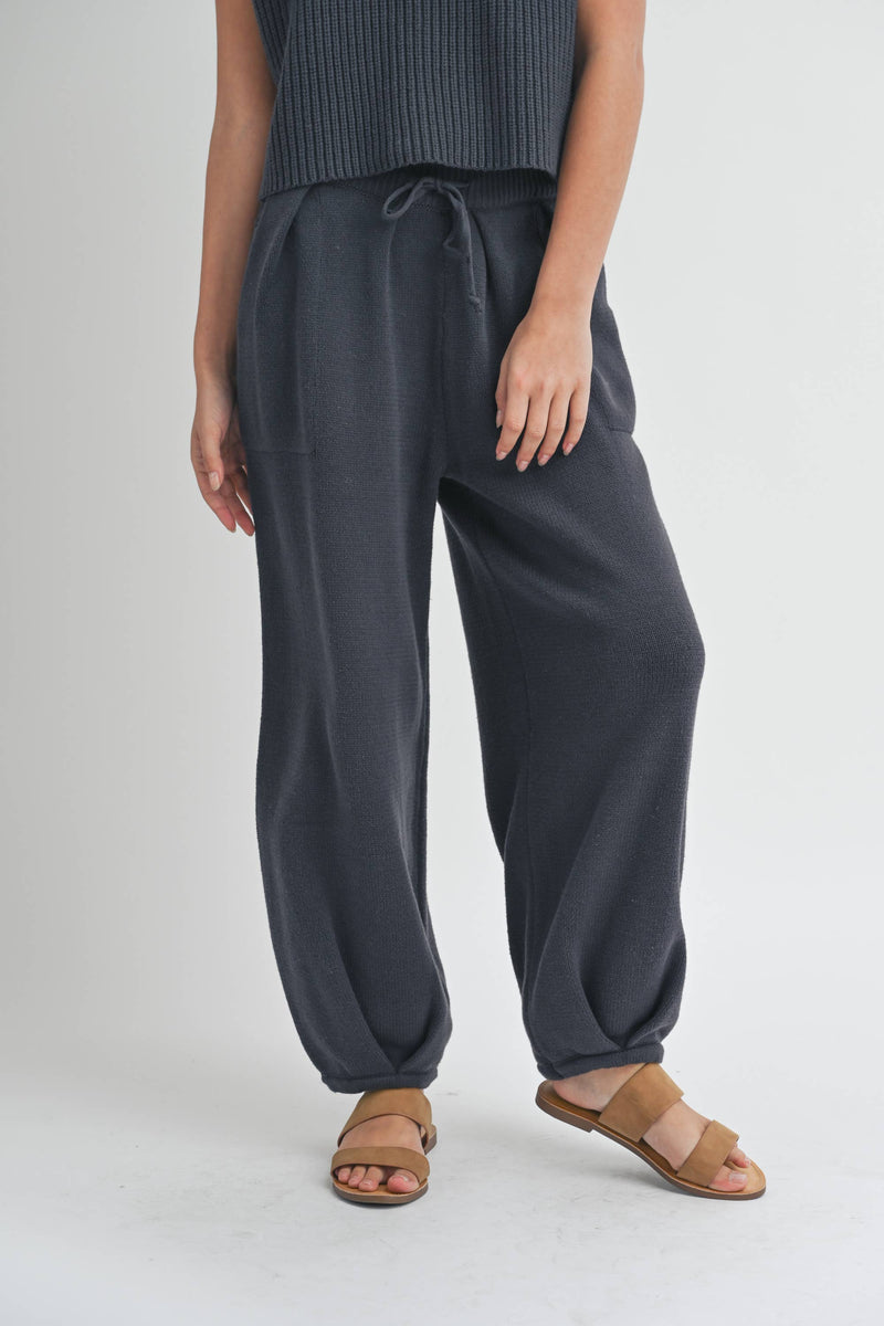 Woman wearing pleated bottom knitted pants in relaxed fit with drawstring waist and ankle detail.