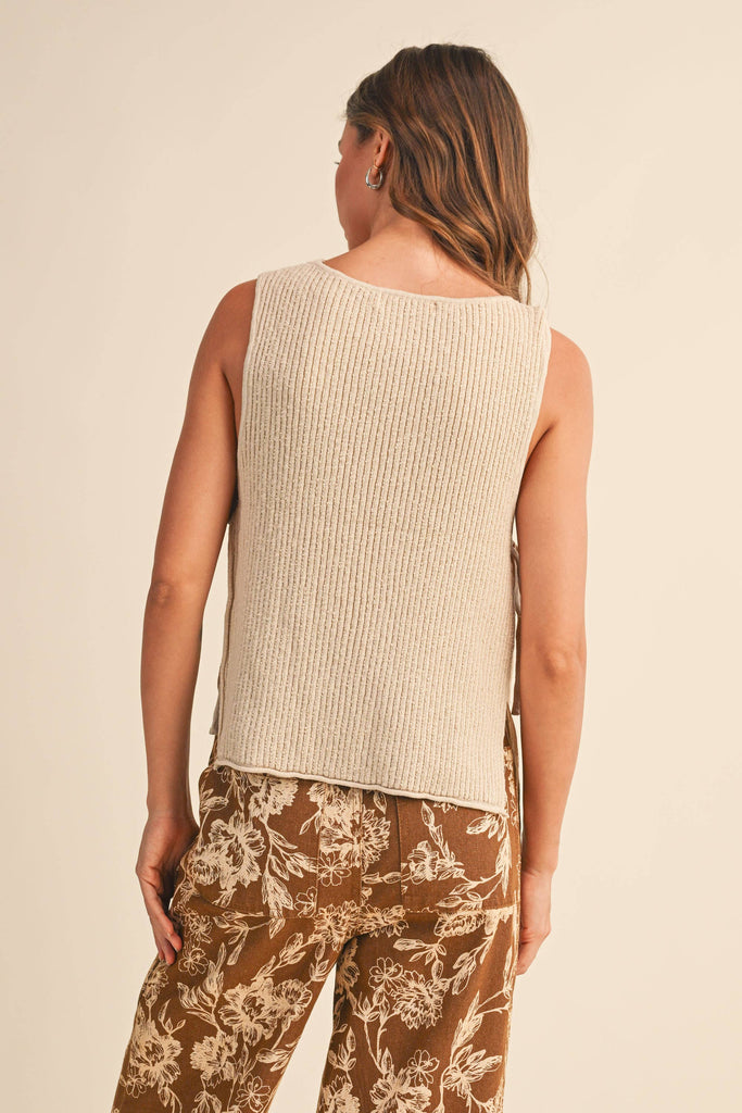 Woman wearing a beige sleeveless top and patterned pants on a beige background