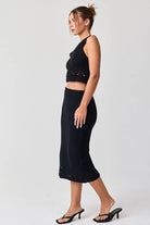 Woman wearing a black sleeveless crochet top and midi skirt set.
