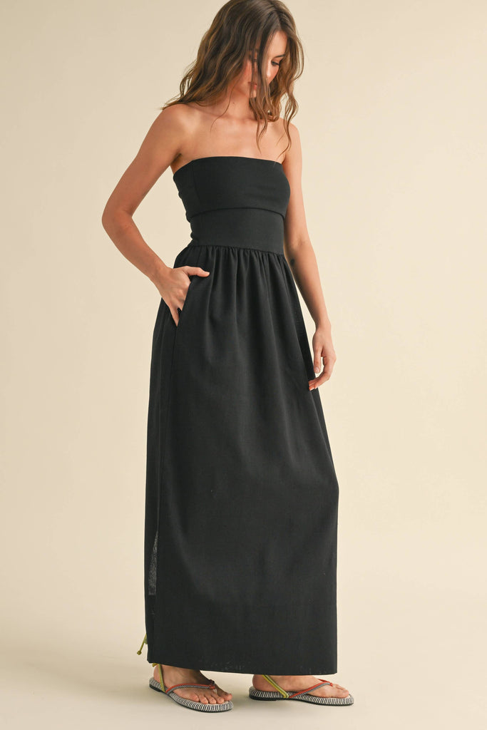 Woman wearing a black strapless maxi dress with a fitted bandeau bodice and flowy skirt.