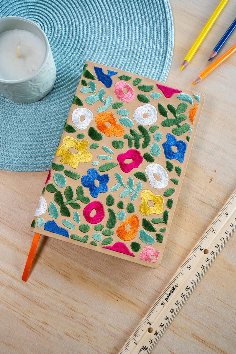 Notebook with floral patterns on a wooden surface with pencils and a candle.