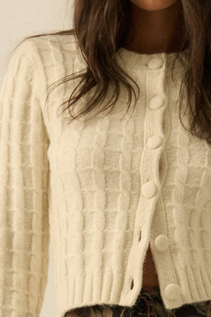 Woman wearing a cream textured knit cardigan with covered buttons, styled with a floral skirt.