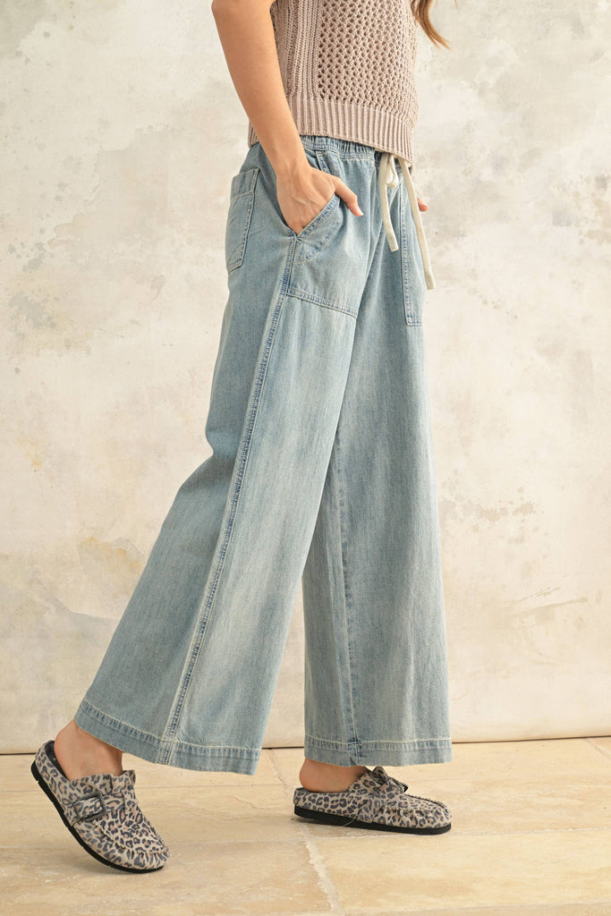 Woman wearing light wash wide-leg denim pants with elastic drawstring waist and front patch pockets.