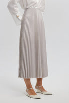 Model wearing a high-waisted pleated maxi skirt styled with a white blouse and pointed heels.