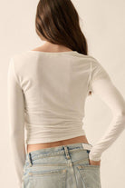 Woman wearing white long-sleeve draped top with asymmetrical ruching.