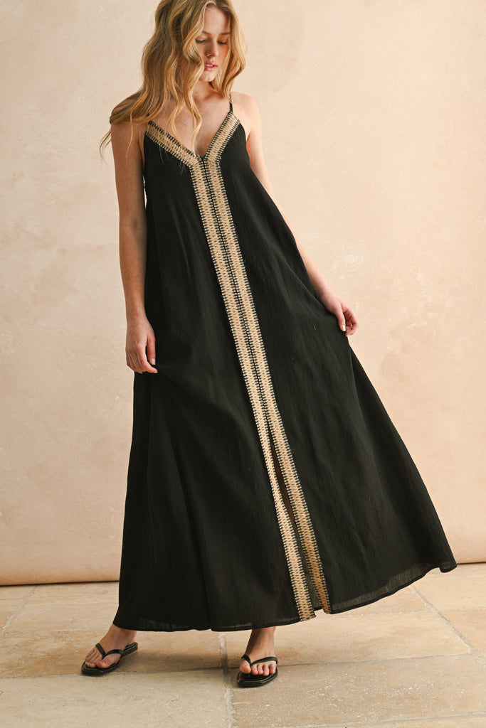Model in black embroidered maxi dress with thin straps and flowy silhouette, featuring beige V-shaped stitching detail.