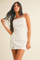 White two-piece set with square-neck top, open back detail, and matching mini skirt with slit, worn by model