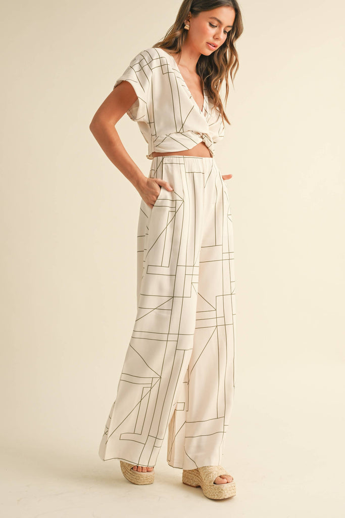 Woman wearing a cream two-piece set with geometric line print, knotted crop top, and wide-leg pants.