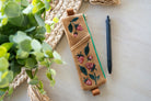 Embroidered strawberry design on a brown pouch with a pen next to it on a light wooden surface.