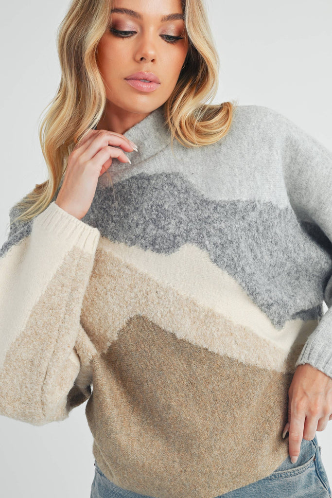 Front and back view of a woman wearing a color-block knit sweater in grey, cream, and taupe with a relaxed fit.