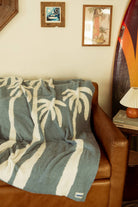 Soft chambray blue plush throw with palm tree design, perfect for cozying up or adding a beachy touch to any space.