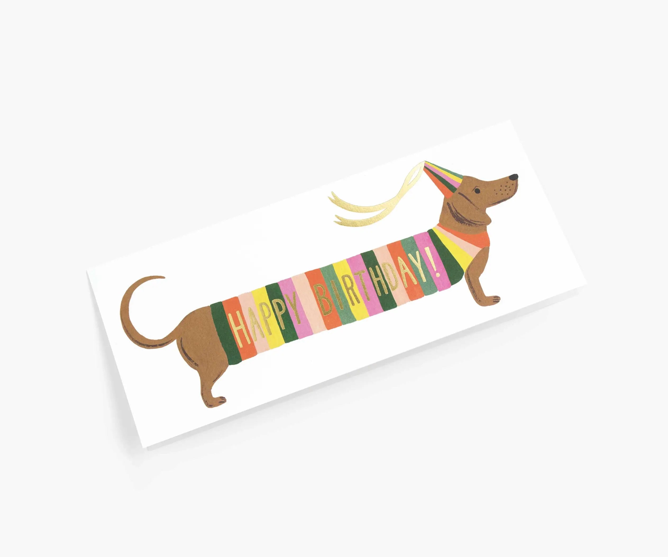Happy Birthday greeting card with a dachshund wearing a colorful striped sweater, gold foil lettering, and a yellow envelope.