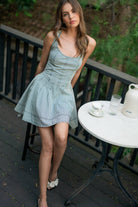 Woman wearing a sleeveless striped mini dress with criss-cross back straps and a large bow tie at the waist.