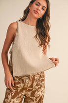 Woman wearing a beige sleeveless top and brown floral pants on a plain background