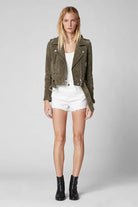Woman wearing a green jacket, white top, and shorts on a gray background