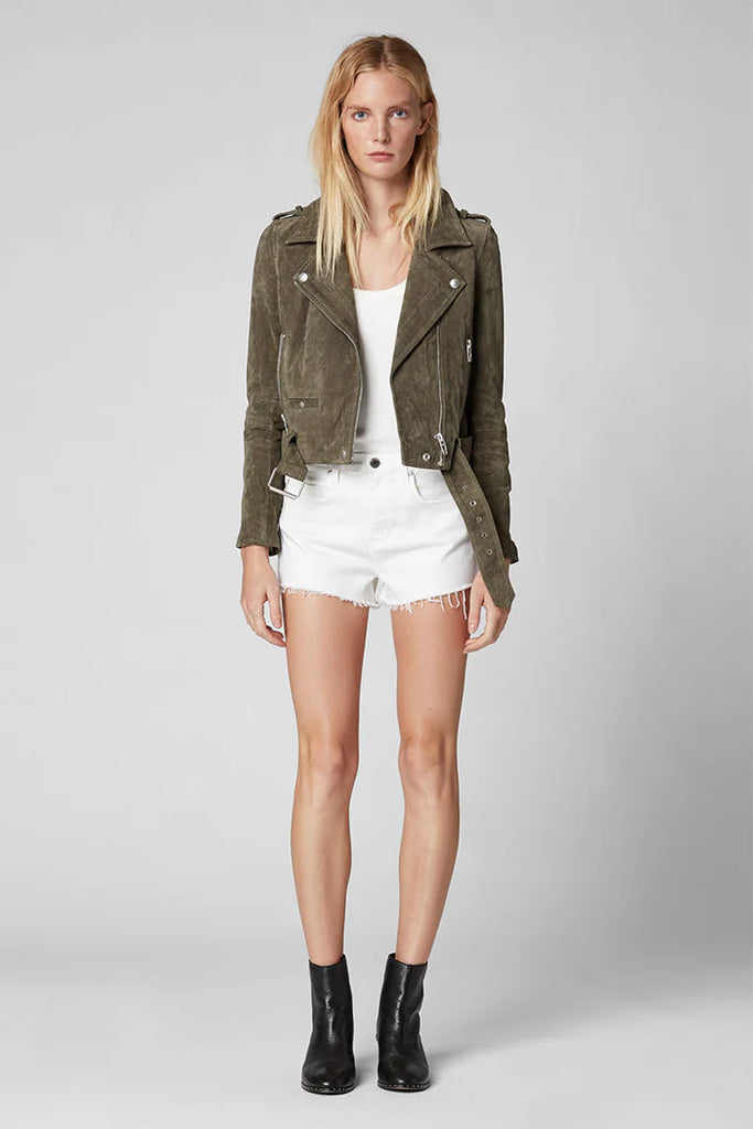 Woman wearing a green jacket, white top, and shorts on a gray background