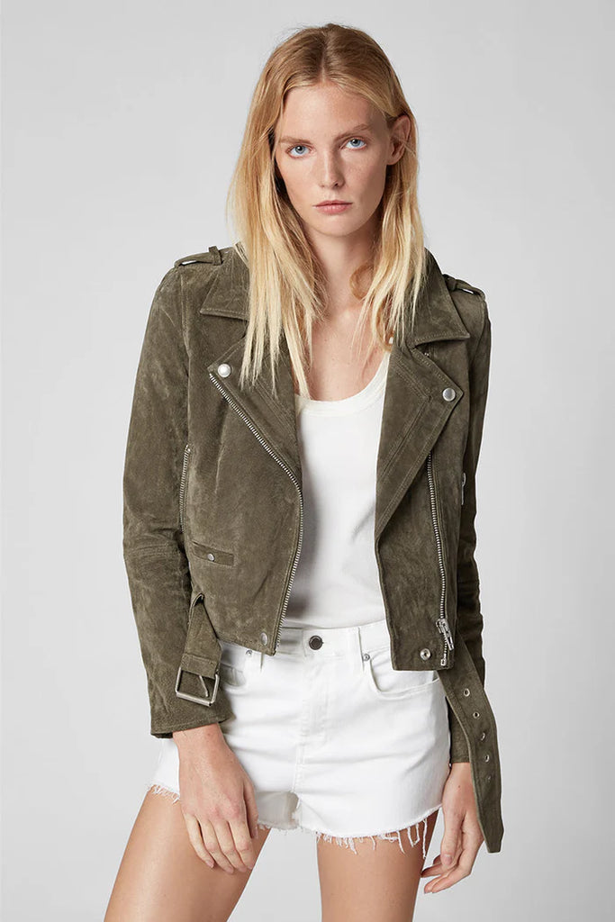 Woman wearing an olive green jacket over a white top and shorts on a light gray background