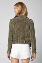 Person wearing a green suede jacket and white shorts on a plain background