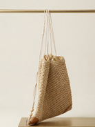 Woven bag with drawstring and tassel on a neutral background