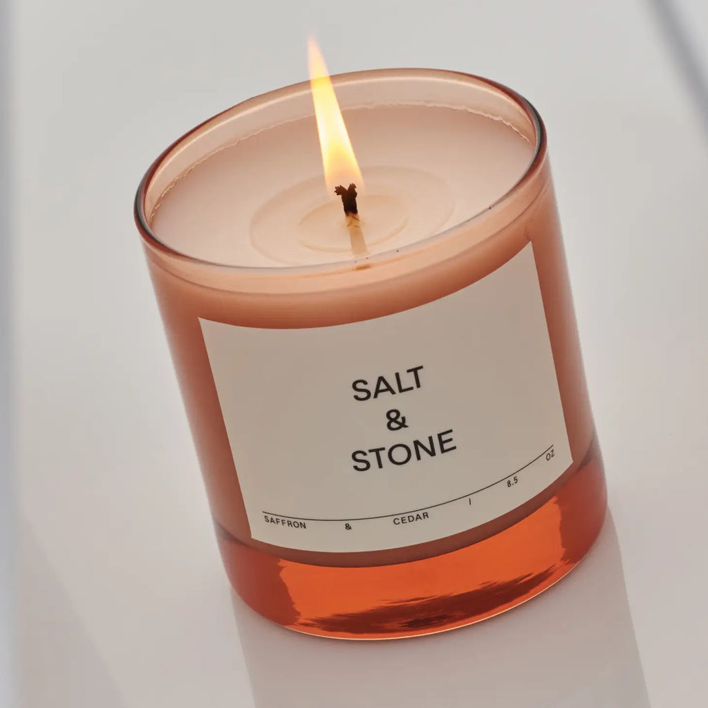 Salt & Stone Candle in Saffron & Cedar, glowing warmly, adding a touch of elegance to the space.