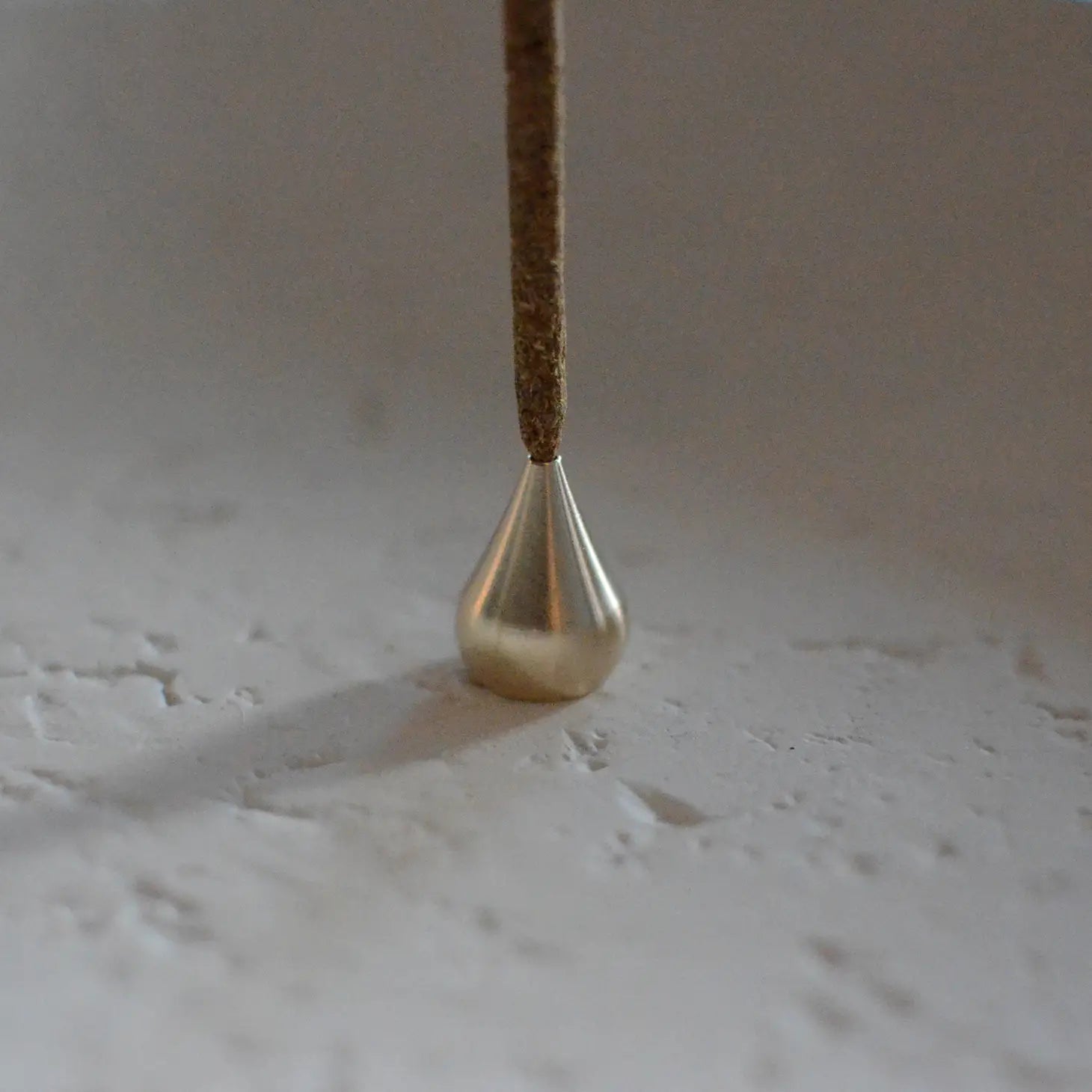 Elegant Brass Water Drop Incense Holder placed on a neutral backdrop, casting a warm glow, ideal for holding incense in style.